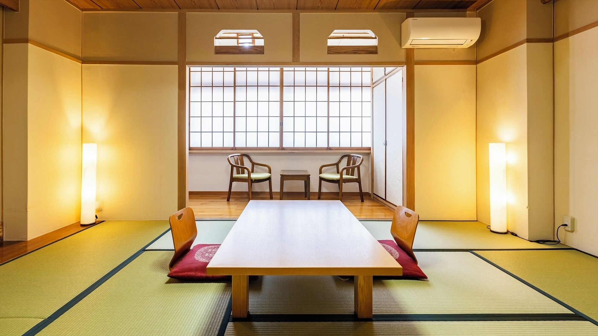 Ett traditionellt japanskt rum med tatamimattor på golvet, ett lågt bord, två stolar och skjutdörrar.