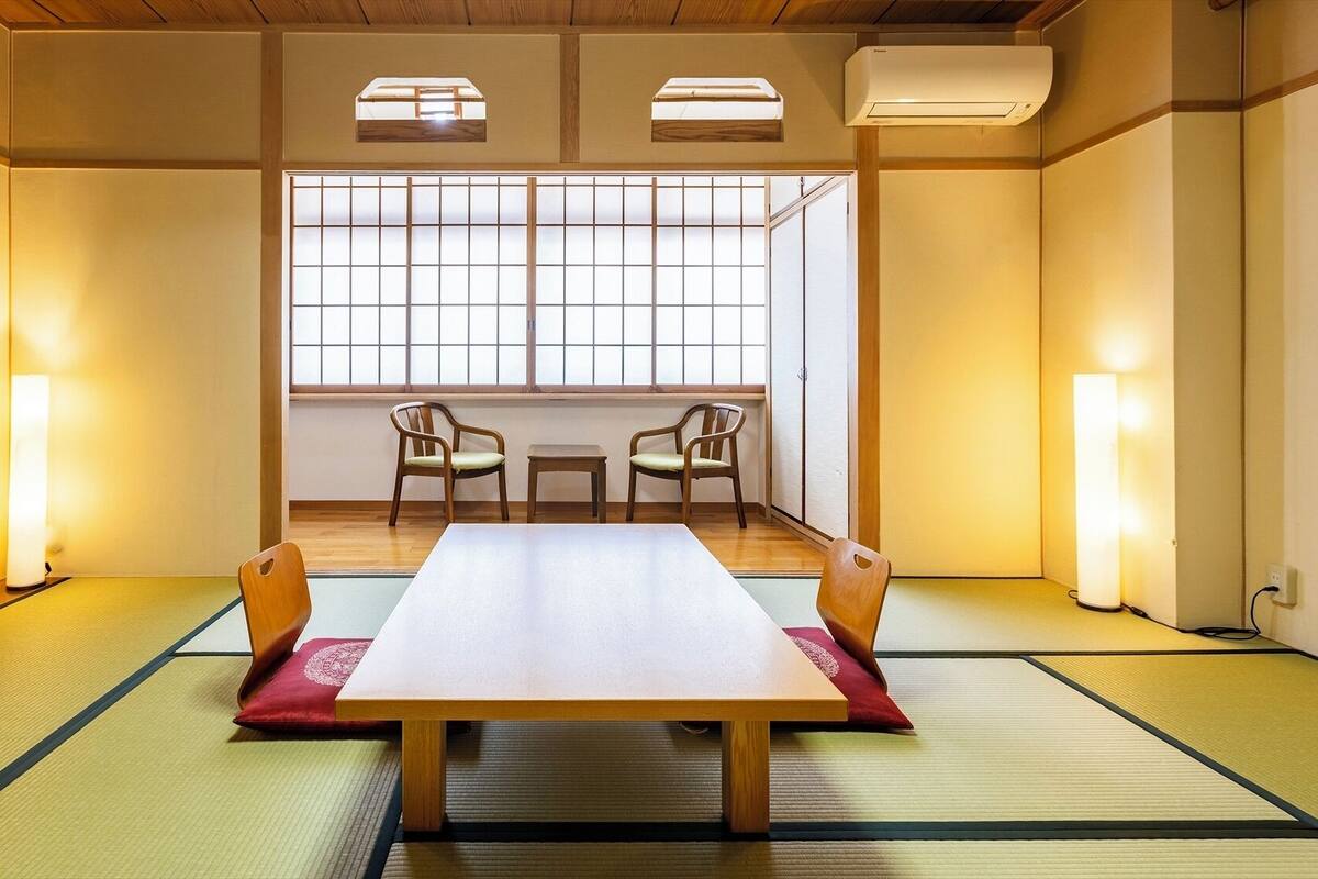 A traditional Japanese room with tatami flooring, a low table, two chairs, and sliding doors.
