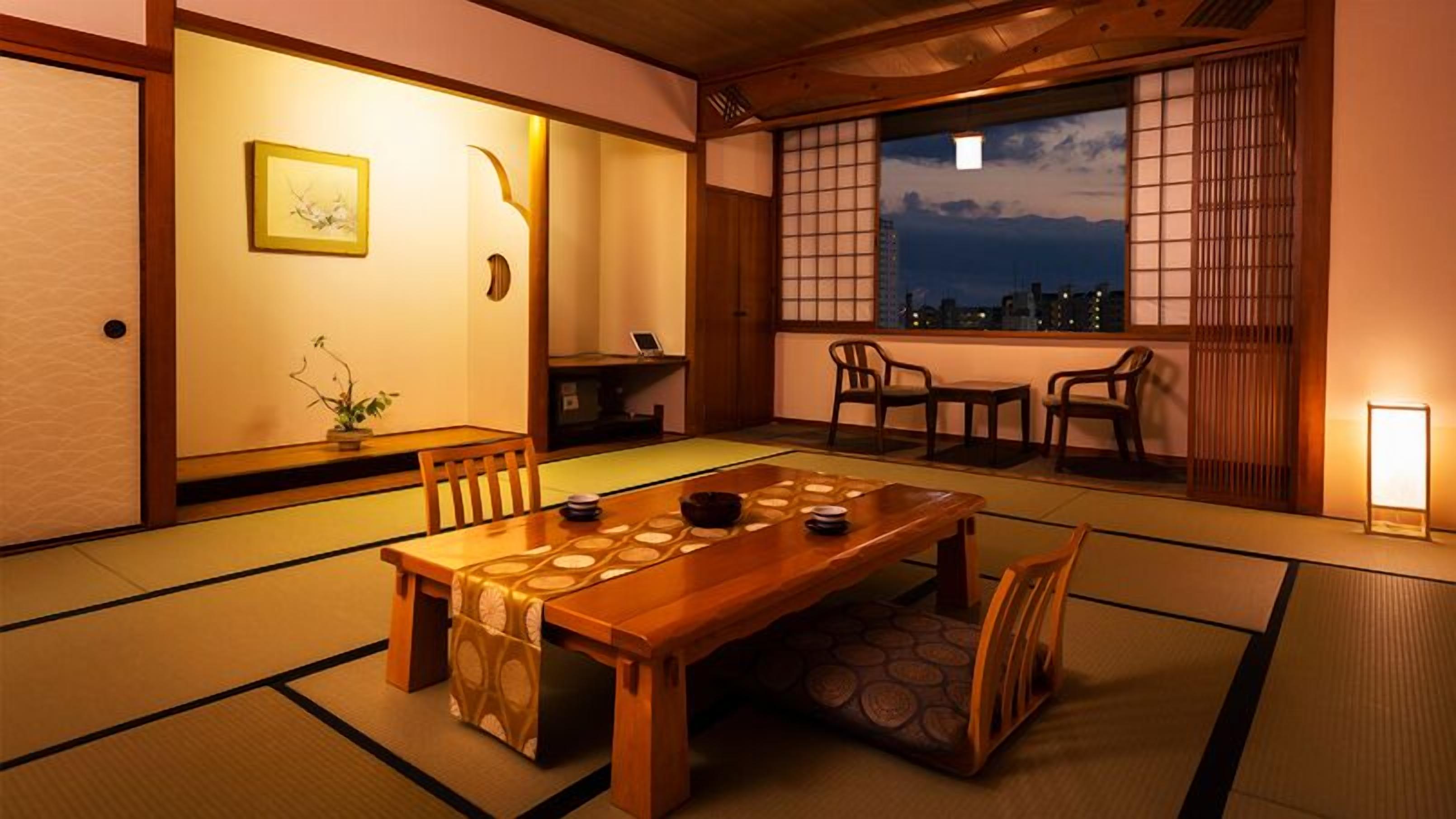 A traditional Japanese room with tatami flooring, a wooden table, and a view of the city at dusk.
