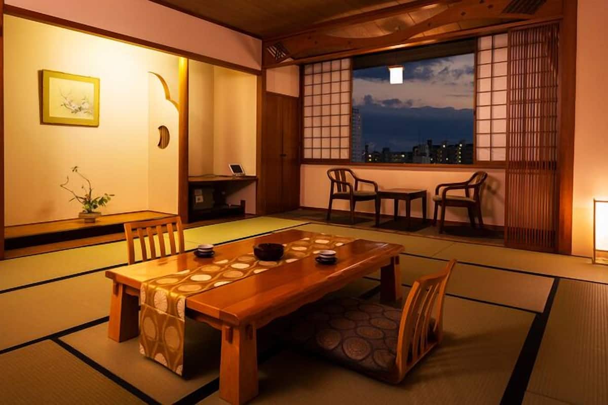 A traditional Japanese room with tatami flooring, a wooden table, and a view of the city at dusk.