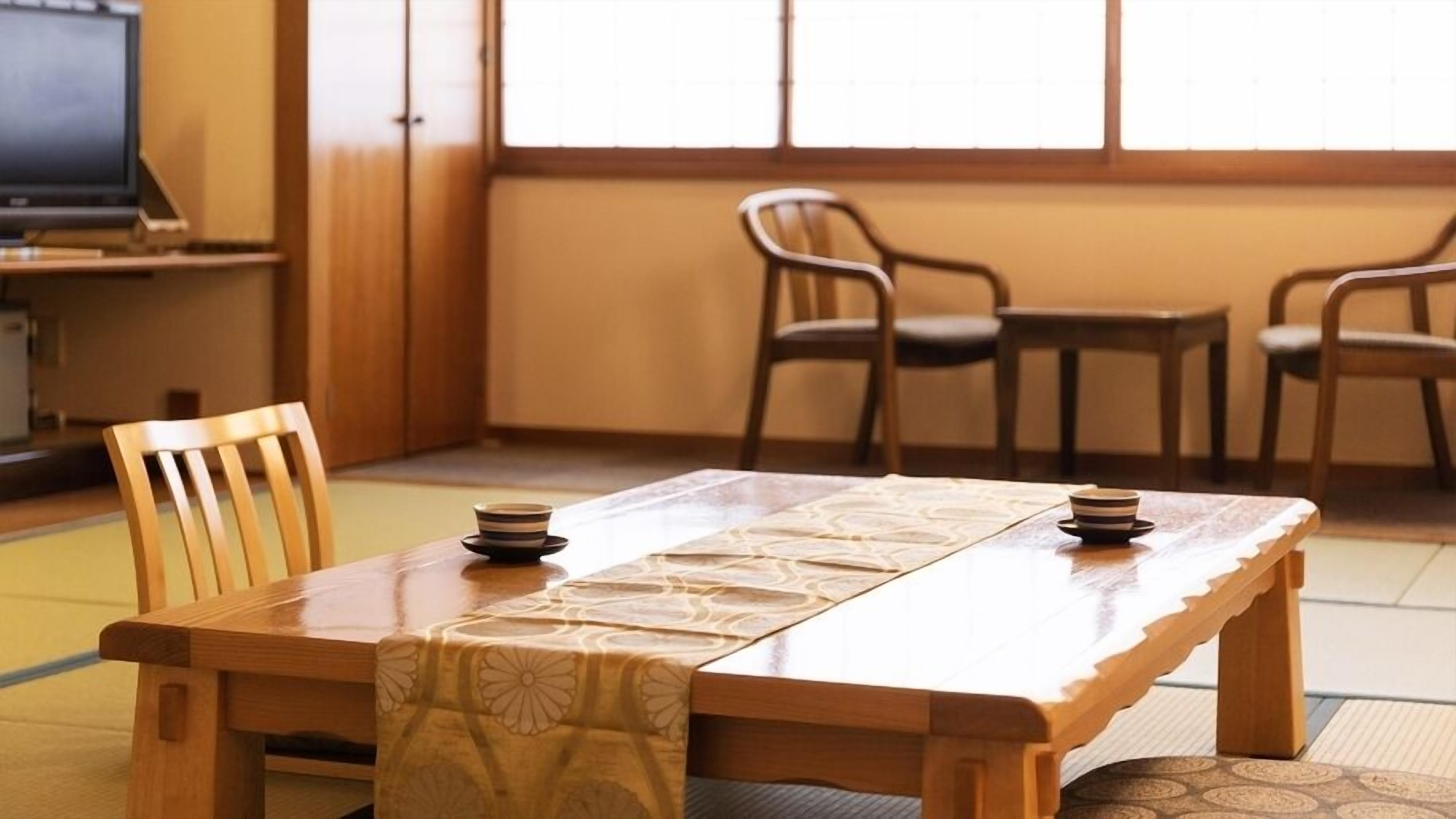 A traditional Japanese room with tatami flooring, a low wooden table, and a television in the background.