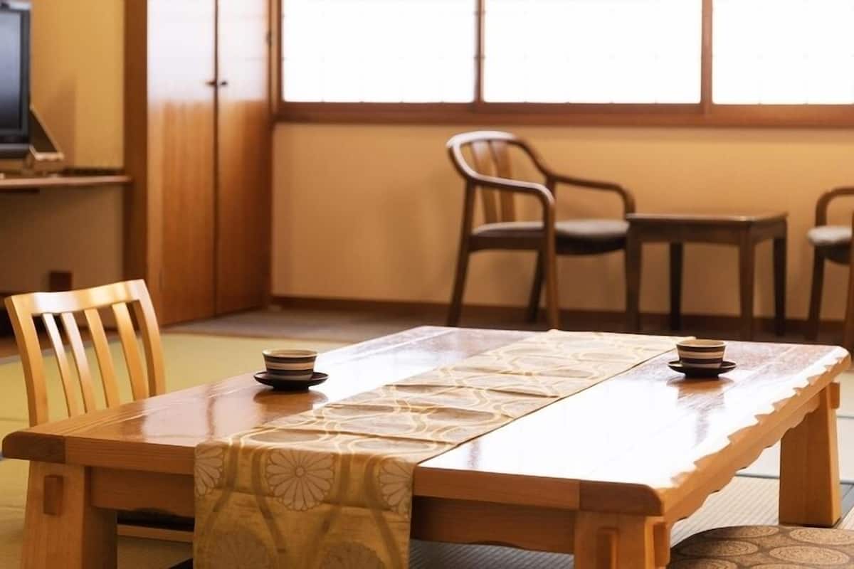 A traditional Japanese room with tatami flooring, a low wooden table, and a television in the background.