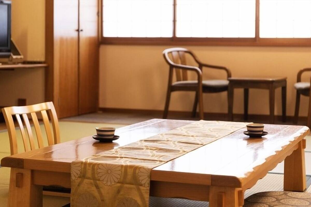 A traditional Japanese room with tatami flooring, a low wooden table, and a television in the background.