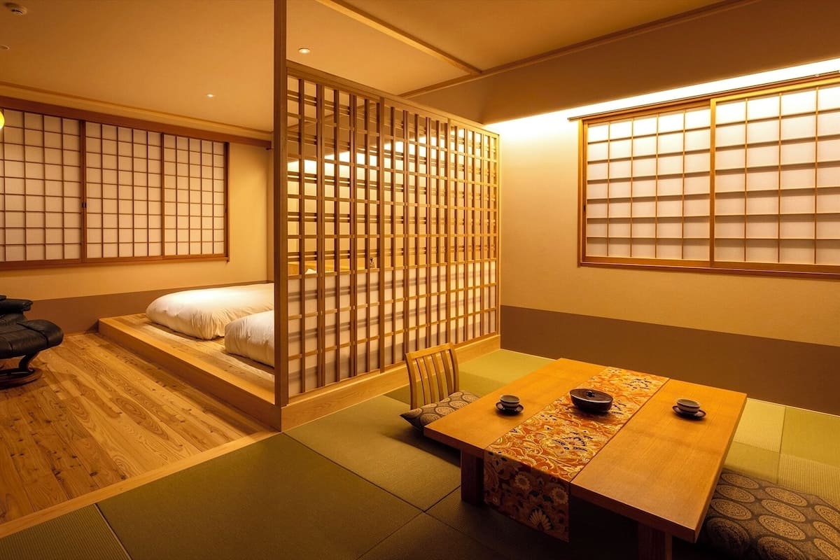 A traditional Japanese room with tatami flooring, a low bed, a wooden table with tea set, and sliding doors.