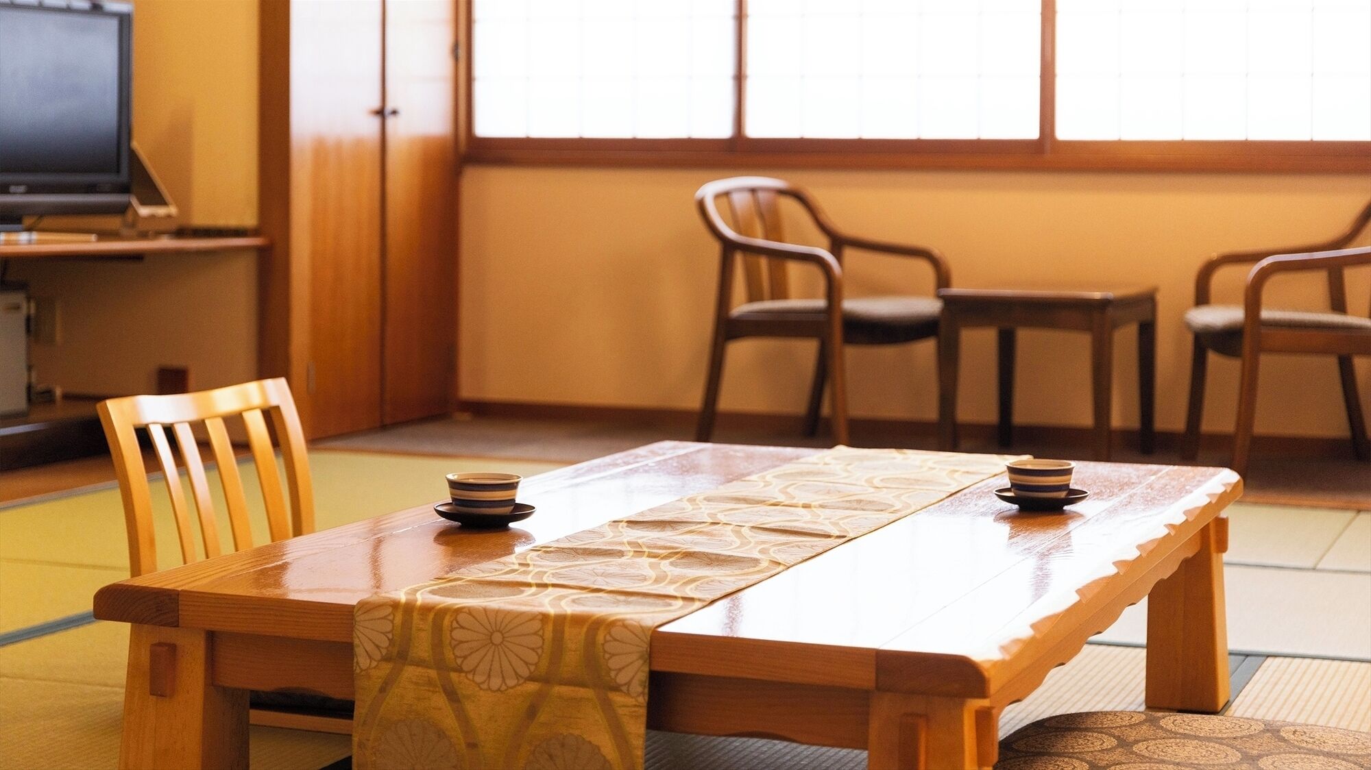 Ett traditionellt japanskt rum med tatamimattor på golvet, ett lågt träbord och en tv i bakgrunden.