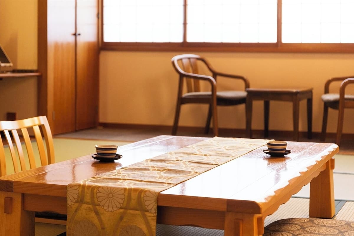 A traditional Japanese room with tatami flooring, a low wooden table, and a television in the background.