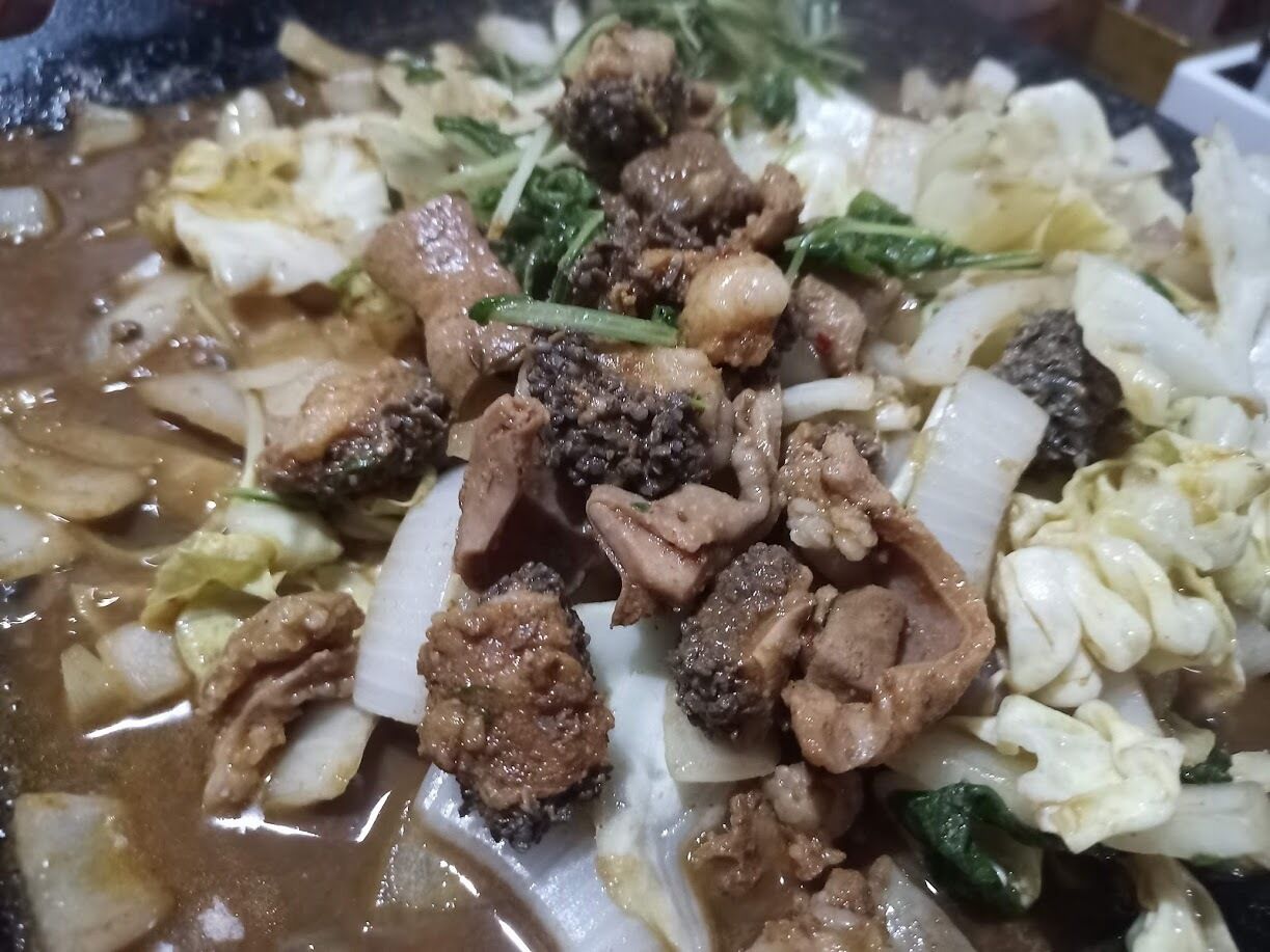 A close-up of a dish with various ingredients, including meat and vegetables in a broth.