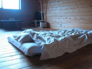 A room with a wooden floor, a bed with white bedding, a small table, and a chair.