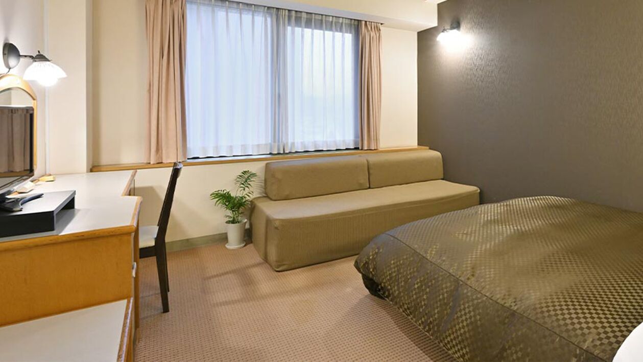 Une chambre d’hôtel avec un lit, un canapé, un bureau avec une lampe et une fenêtre avec des rideaux.