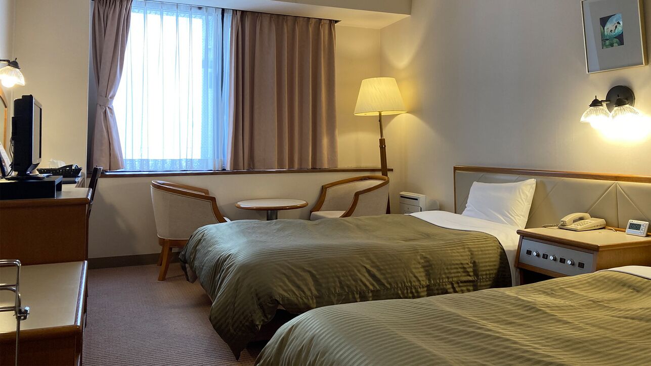 Une chambre d’hôtel avec deux lits, un bureau, une chaise, une lampe et une table de chevet avec un téléphone.