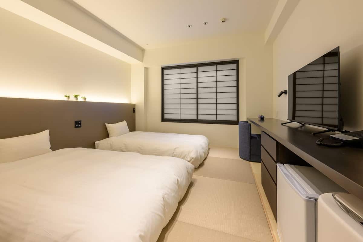 Hotellihuone, jossa on kaksi sänkyä, työpöytä tietokoneella, televisio ja ikkuna, josta on näkymä.