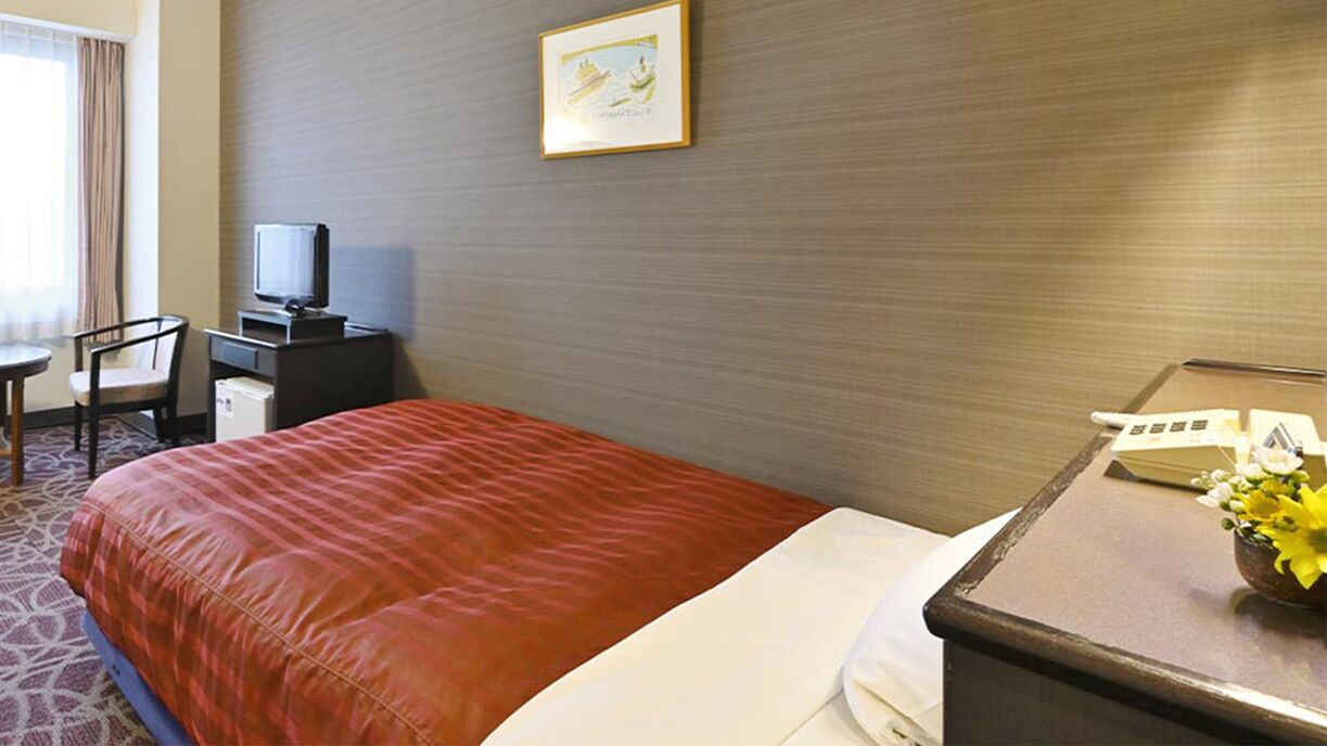 Une chambre d’hôtel comprenant un lit, un bureau avec un téléphone, une télévision, une chaise et une fenêtre avec des rideaux.