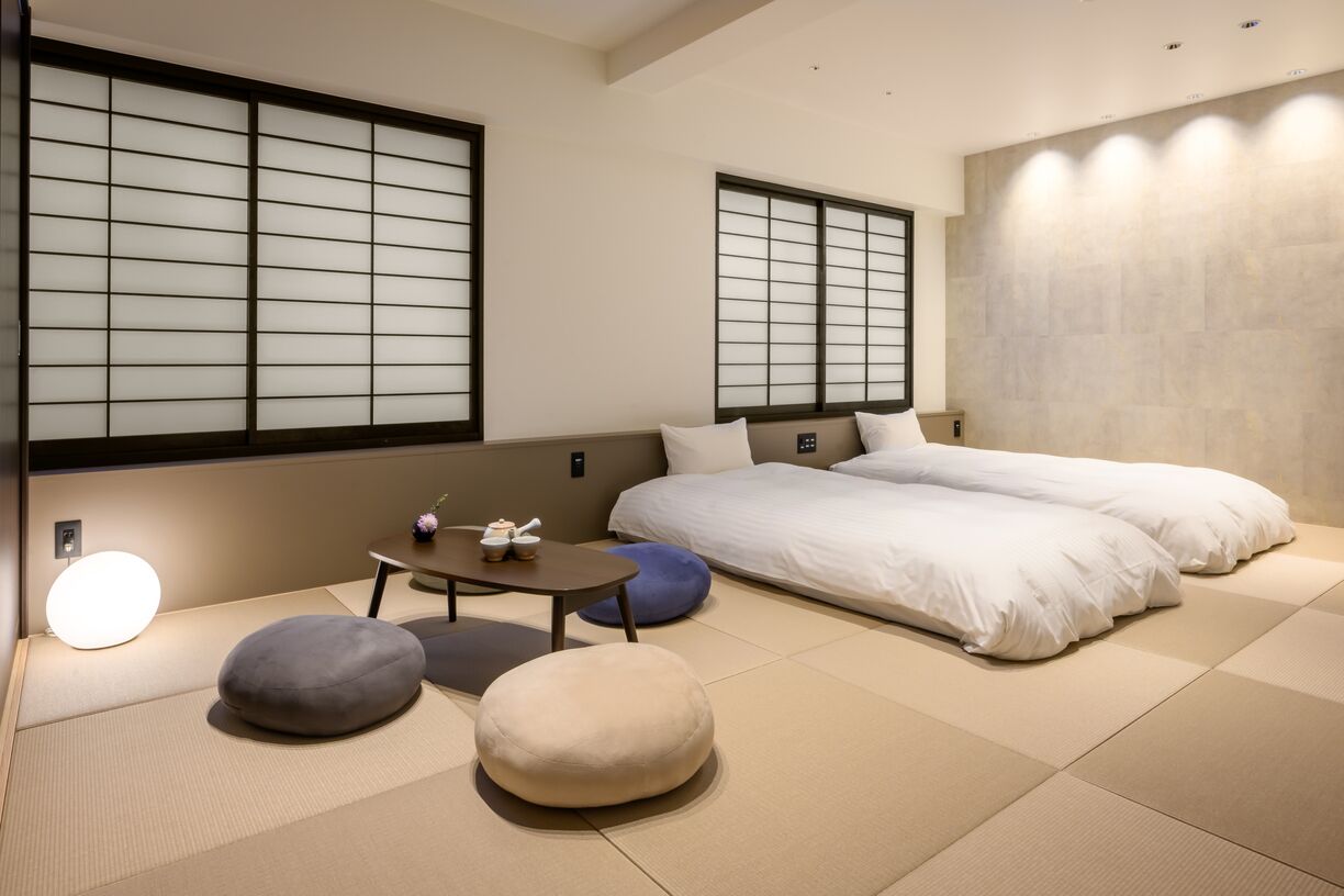 Perinteinen japanilaistyylinen huone, jossa on tatamimatto, kaksi sänkyä, pieni pöytä ja liukuvat ovet.