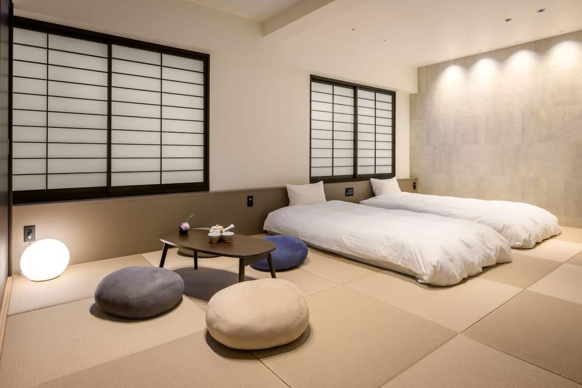 Perinteinen japanilaistyylinen huone, jossa on tatamimatto, kaksi sänkyä, pieni pöytä ja liukuvat ovet.