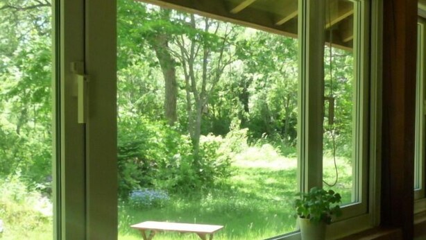 Ein Zimmer mit großem Fenster, das einen Blick auf eine Rasenfläche mit Bäumen und einem Picknicktisch bietet.