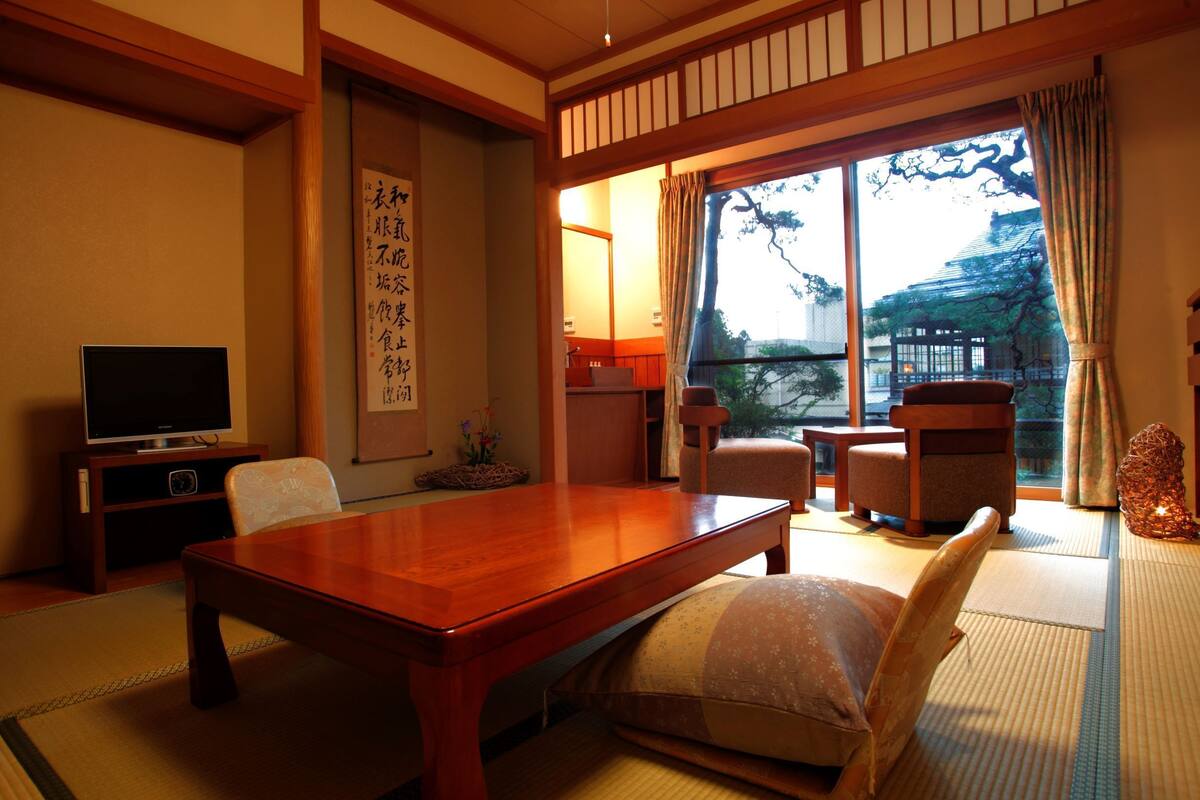 A traditional Japanese room with tatami flooring, a wooden table, and a television on a low stand.