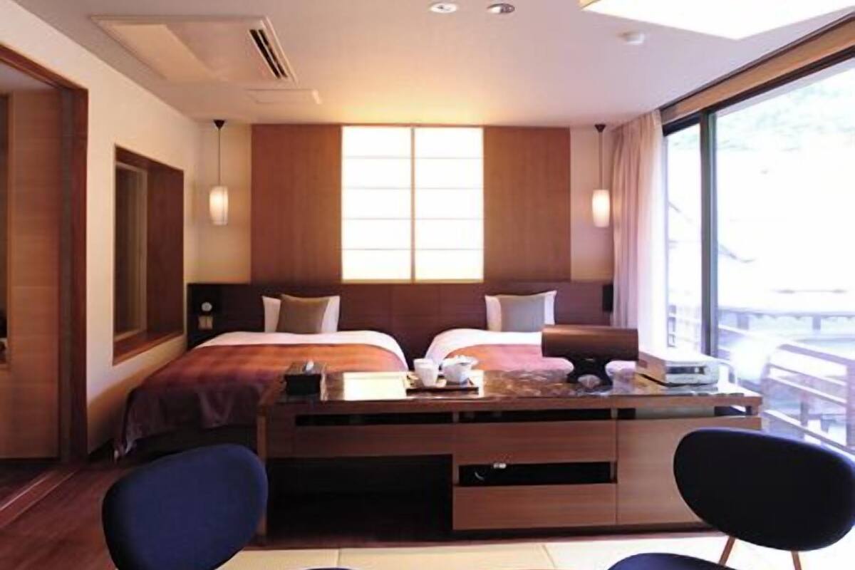 A hotel room with a bed, bedside tables, a desk, two chairs, and a large window.