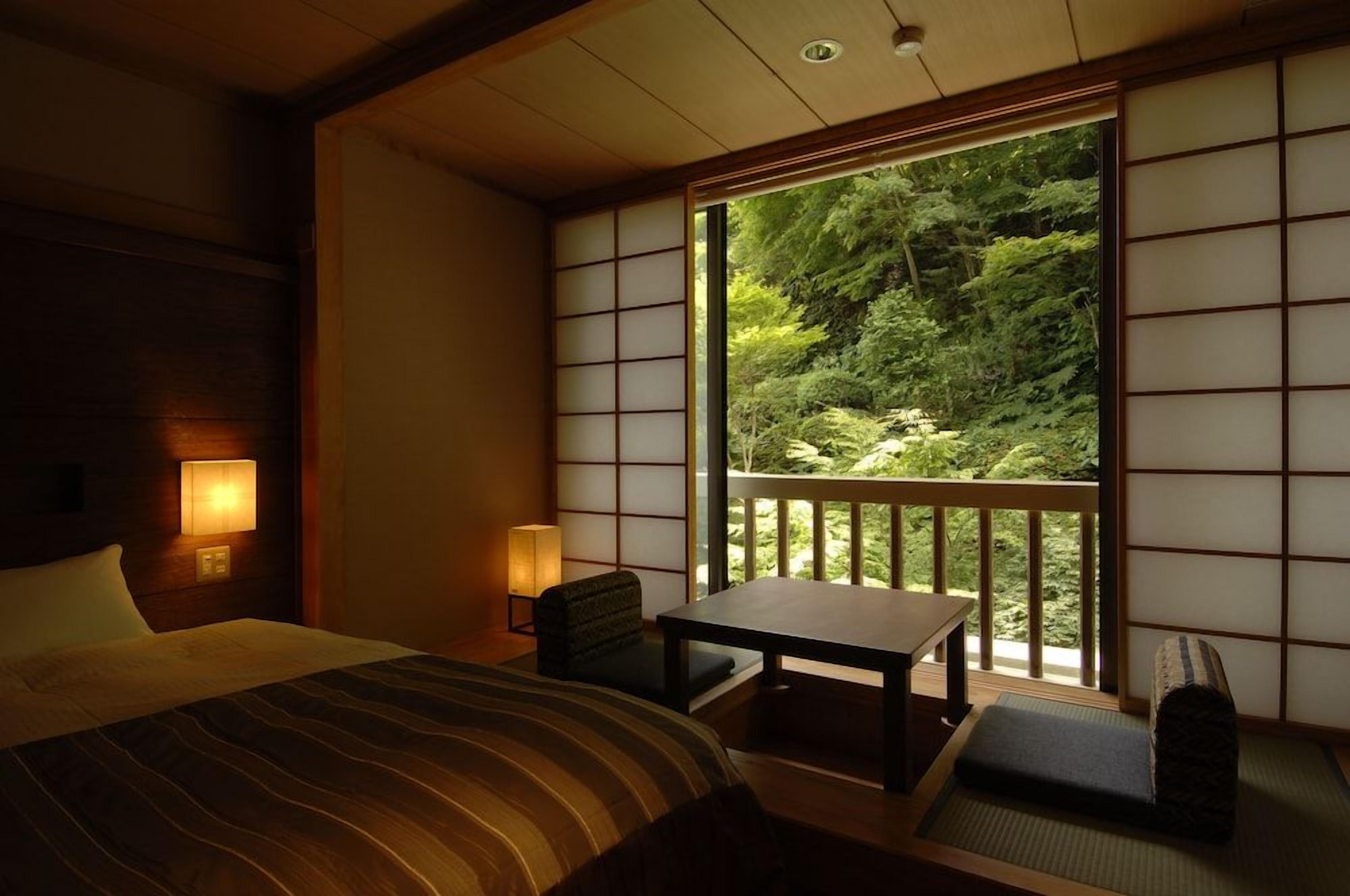 A traditional Japanese-style room with tatami flooring, a low table, and a bed with a striped bedspread.