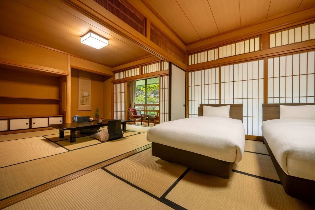 A traditional Japanese-style room with tatami flooring, a low table, two beds, and shoji screens.