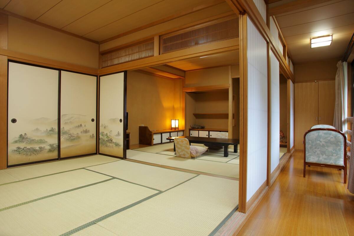 A traditional Japanese room with tatami flooring, sliding doors, a low table, and a chair.