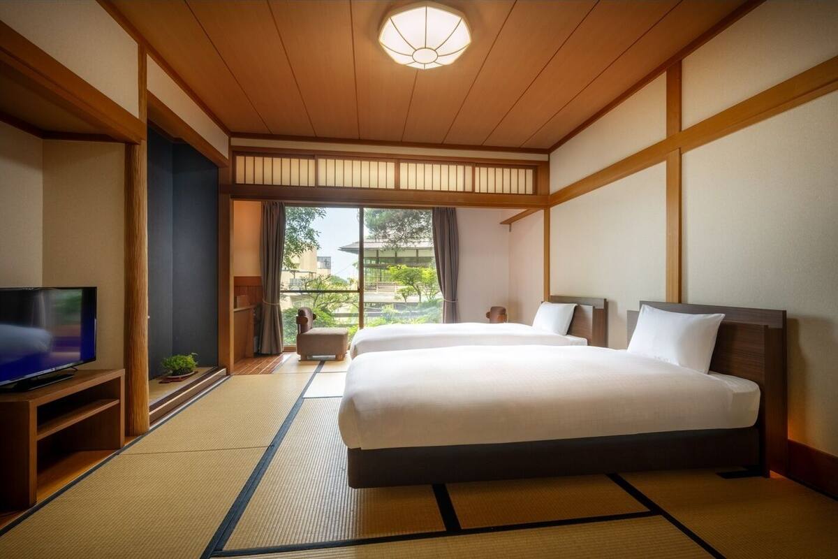 A hotel room with a large bed, a television, and a view of greenery outside.