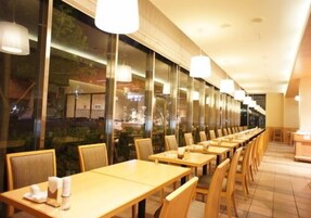 Un restaurante con mesas y sillas largas, ventanas amplias e iluminación colgante.