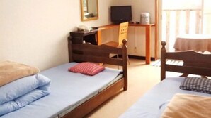 Ein Zimmer mit zwei Einzelbetten, einem Schreibtisch mit Stuhl, einem Fernseher und einer Klimaanlage.