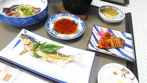 Ein Esstisch mit verschiedenen Gerichten, darunter Fisch, Suppenschüsseln und einem heißen Topf.