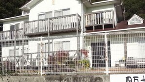 Ein weißes Gebäude mit Balkon, einem eingezäunten Bereich und einem Schild mit japanischen Schriftzeichen.