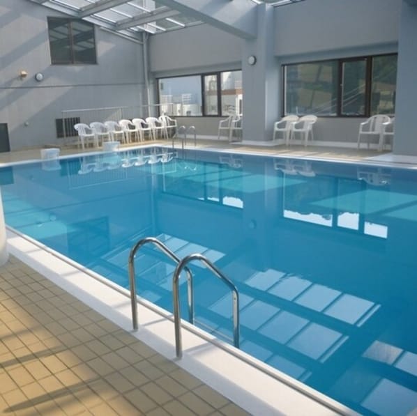 An indoor swimming pool with clear blue water, surrounded by white chairs and a tiled floor. - Bay Resort Hotel Naruto Kaigetsu (Naruto)