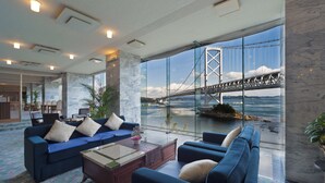 A modern hotel lobby with a large glass window offering a view of a bridge and water. - Bay Resort Hotel Naruto Kaigetsu (Naruto)