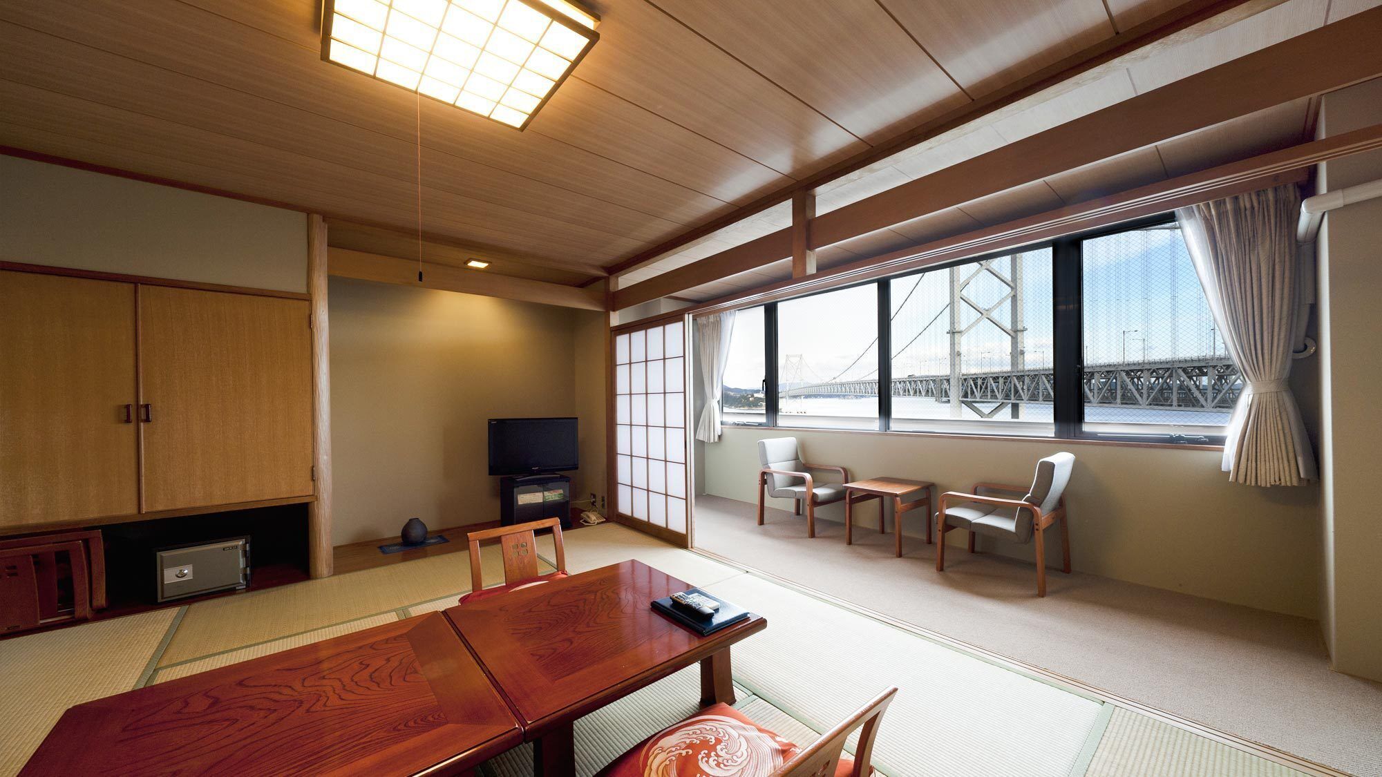 Ein traditioneller japanischer Raum mit Tatami-Boden, einem niedrigen Tisch, Stühlen, einem Fernseher und Blick auf eine Brücke.