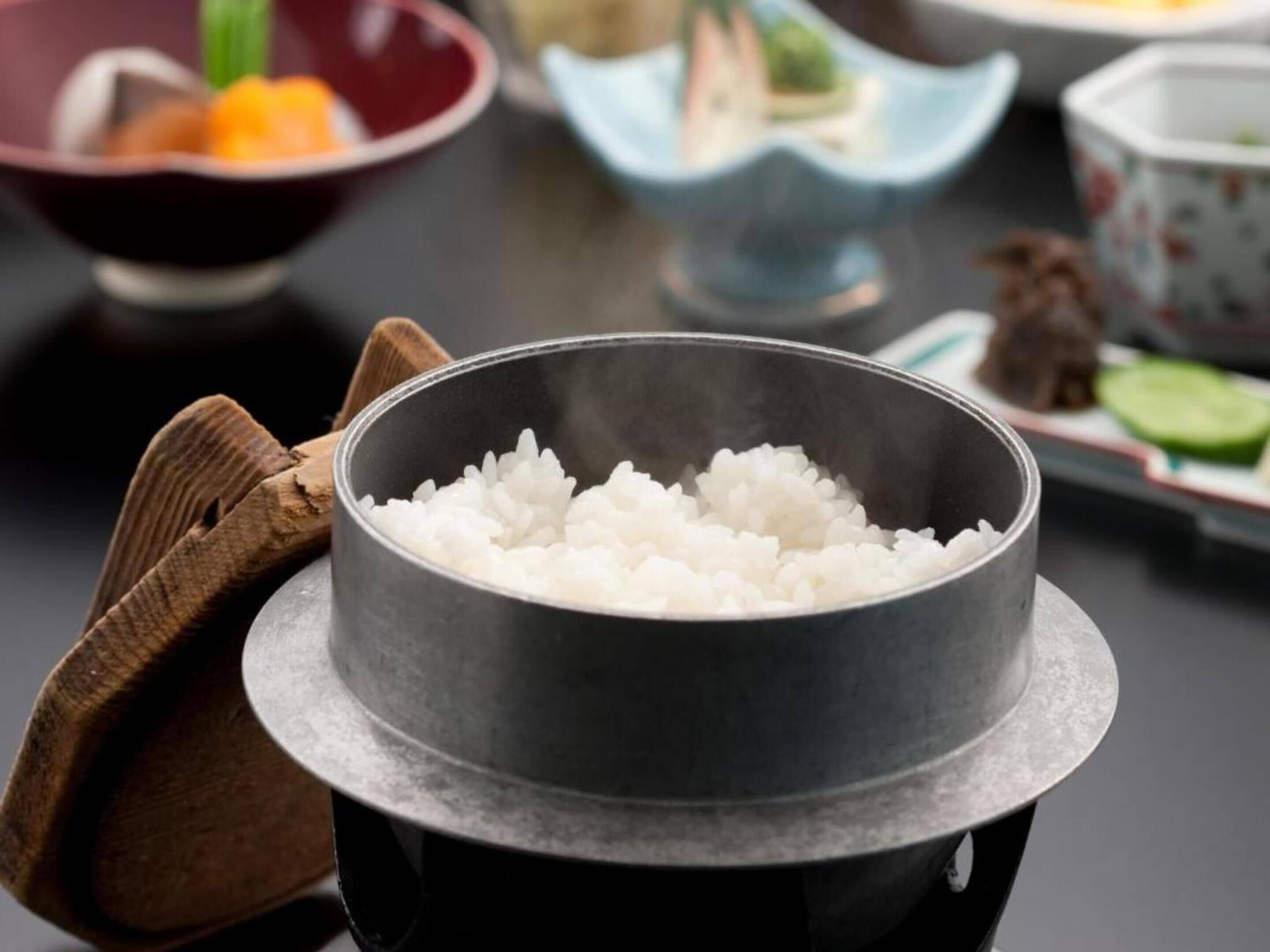 Un tazón de metal con arroz blanco cocido sobre un plato negro.