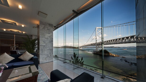 A modern living room with a large glass window overlooking a bridge and water. - Bay Resort Hotel Naruto Kaigetsu (Naruto)
