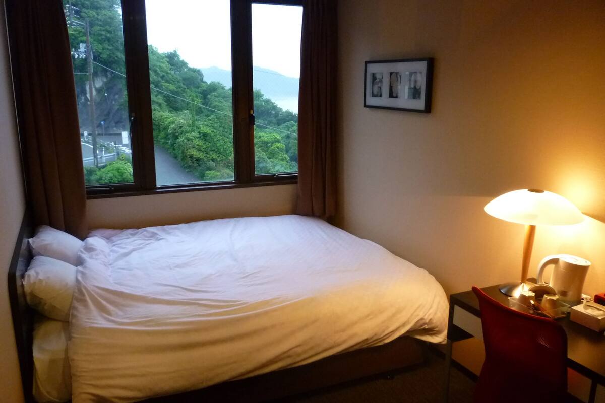 A single bed with white bedding, a nightstand with a lamp, and a framed picture on the wall.