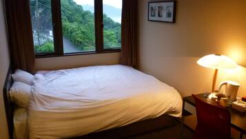 Una cama individual con ropa de cama blanca, una mesita de noche con lámpara y un cuadro en la pared.