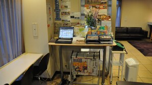 Un mostrador de recepción con una computadora, folletos y un florero. Se observa un sofá de cuero negro y una silla blanca al fondo.