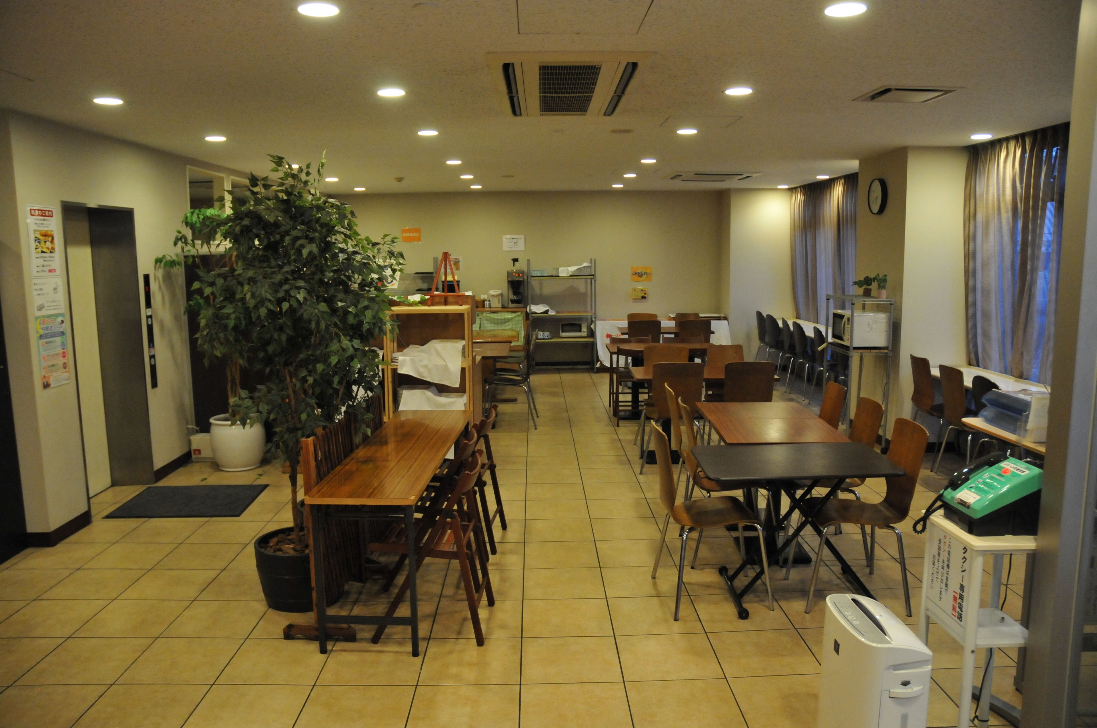 A restaurant with multiple tables and chairs, a large potted plant, and a coffee machine.