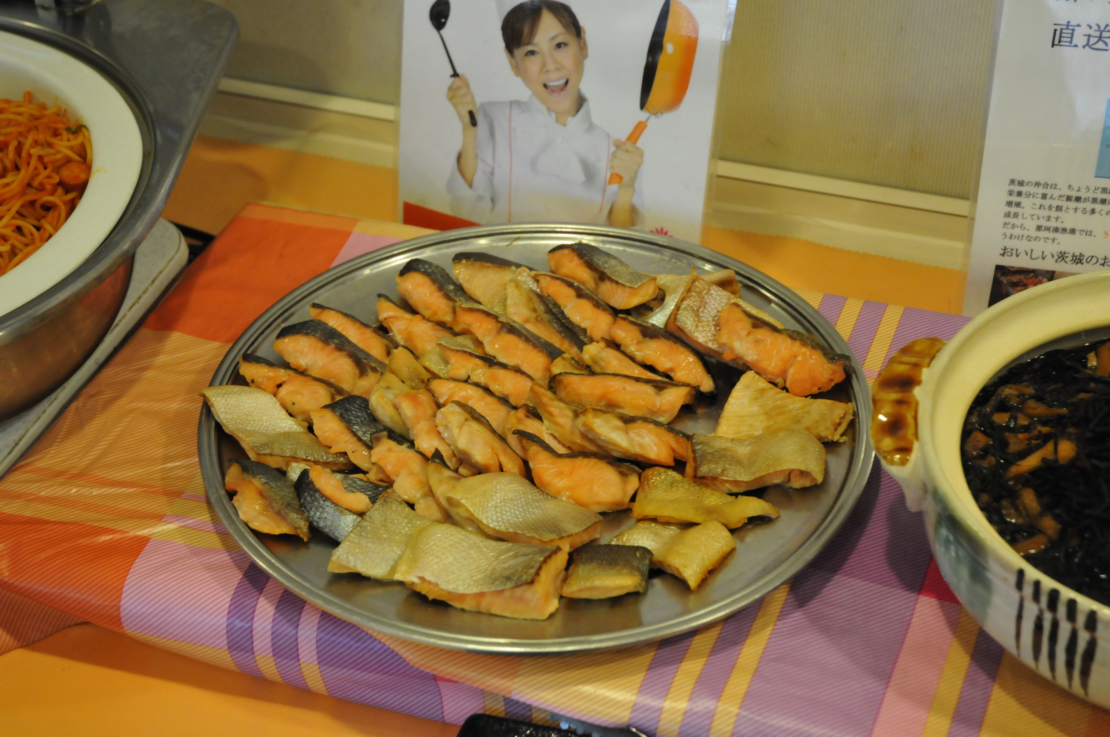 A buffet table with a variety of dishes including fish, noodles, and a bowl of what appears to be pickled vegetables.