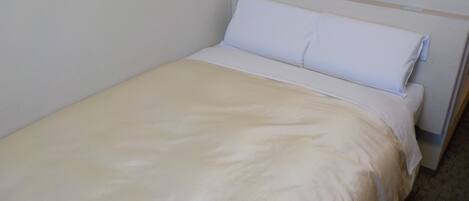 Una habitación pequeña con una cama individual, cubierta con una colcha blanca sencilla y almohadas.