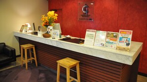 Un mostrador de recepción de hotel con encimera de mármol, taburetes de madera, un jarrón de flores y folletos informativos.