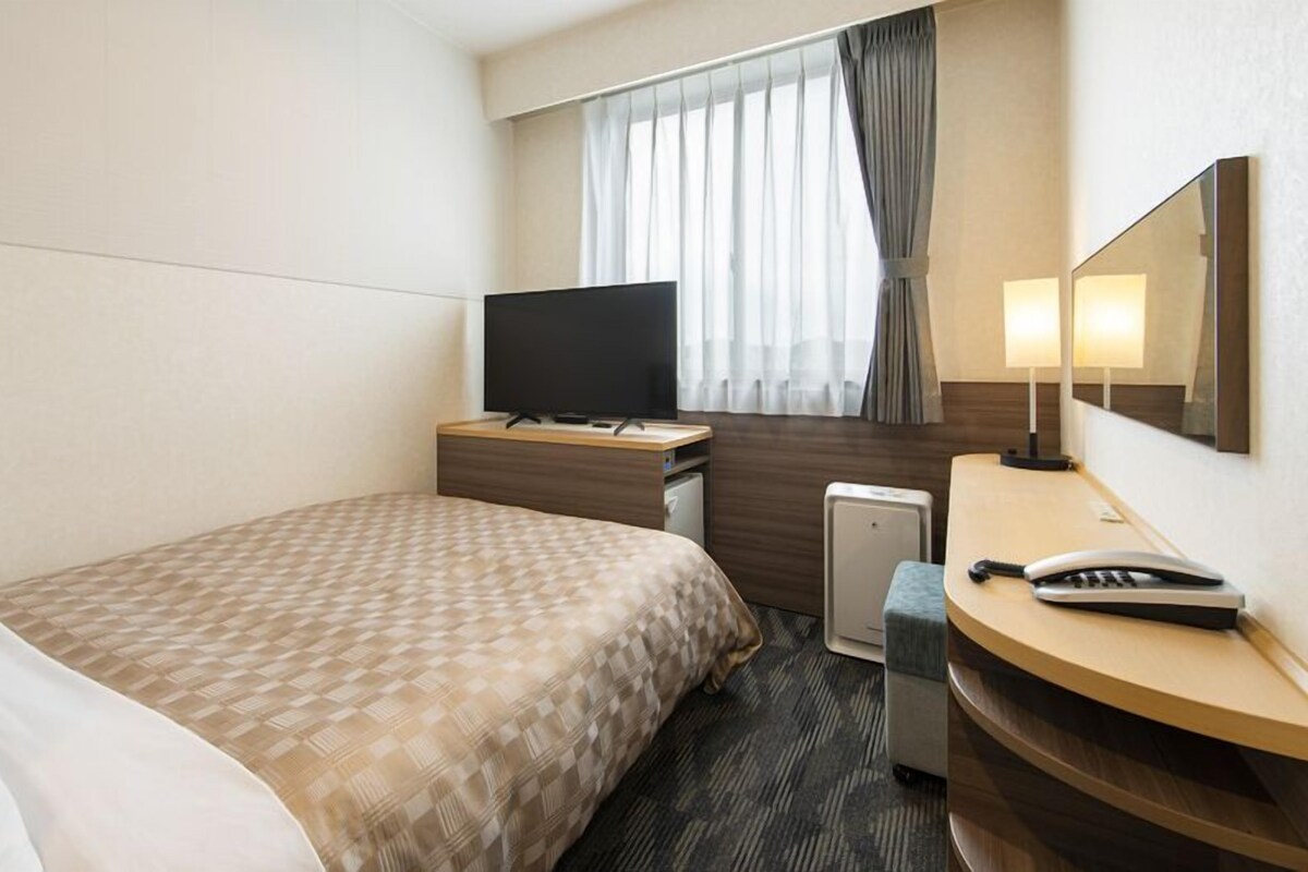 Une chambre d’hôtel comprenant un lit, un bureau avec une télévision, un miroir, une lampe et un téléphone.