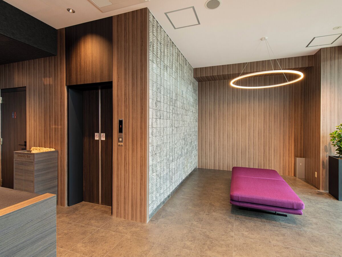 A modern lobby with a reception desk, elevator, and a purple seating area.