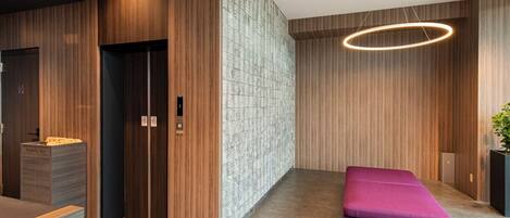 A modern lobby with a reception desk, elevator, and a purple seating area.