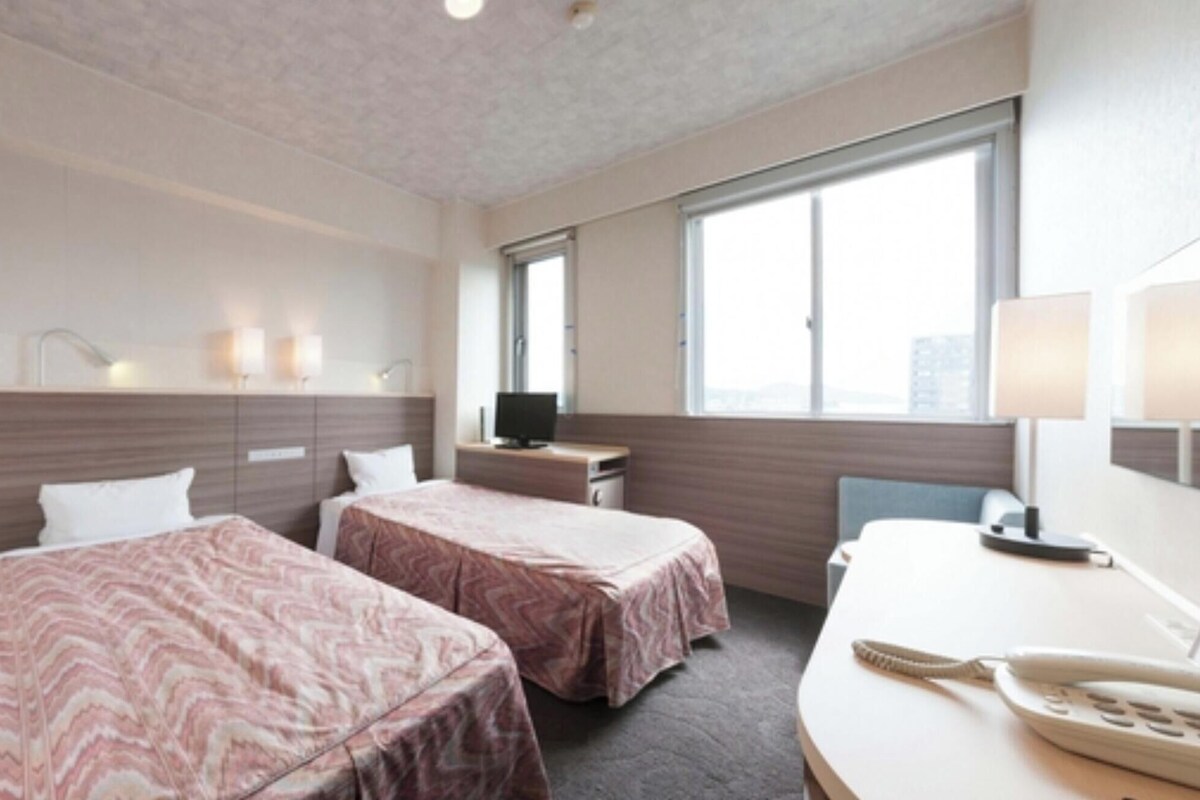 Une chambre d’hôtel avec deux lits, un bureau avec un téléphone, une télévision et une fenêtre donnant sur un beau paysage.