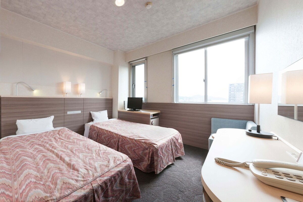 Une chambre d’hôtel avec deux lits, un bureau, un ordinateur, un téléphone et une fenêtre donnant sur la ville.