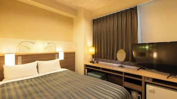 A hotel room with a bed, a desk with a television, a mirror, and a small refrigerator.