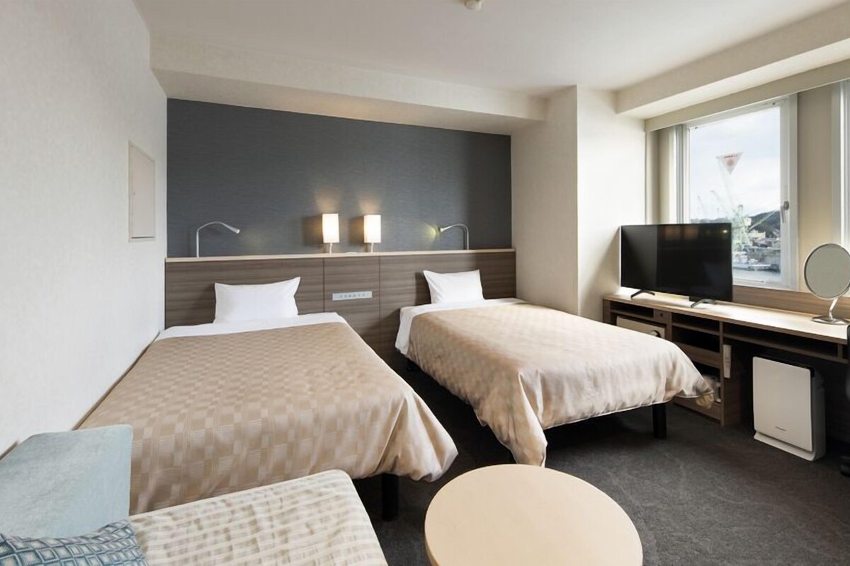 Une chambre d’hôtel avec deux lits, un bureau avec une télévision, une chaise et une vue sur la ville.