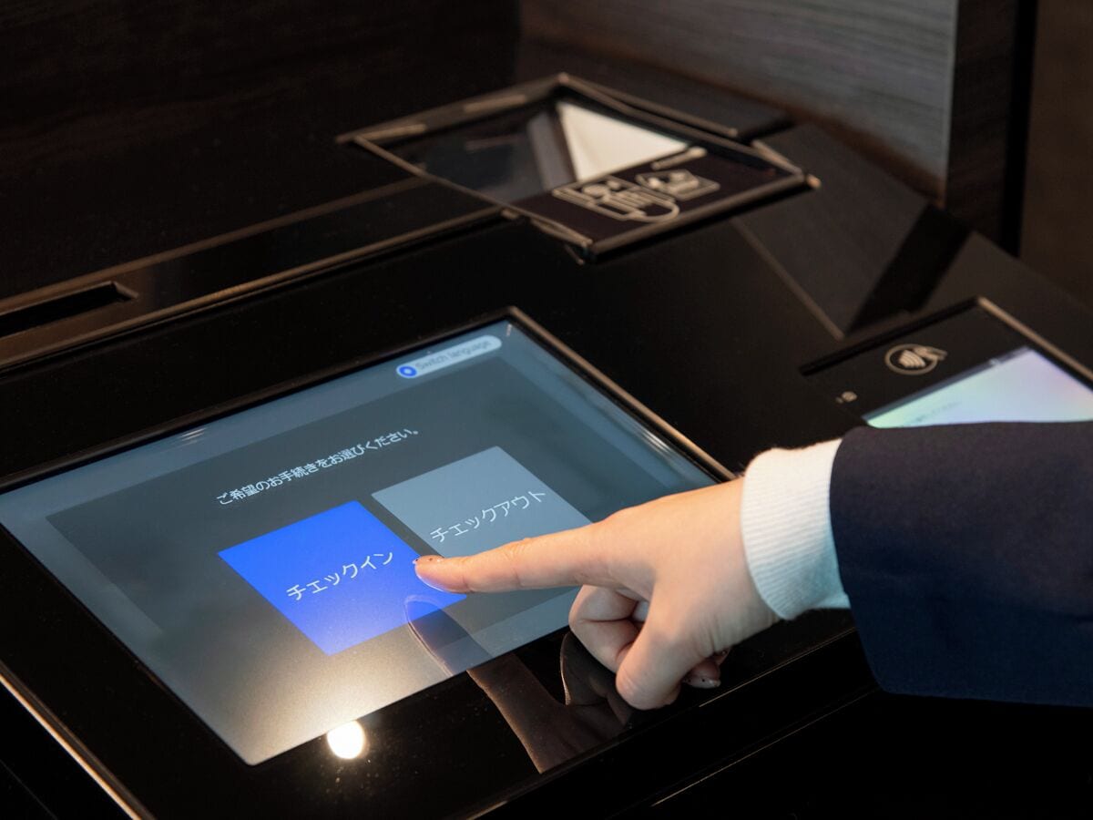 A digital interface on a kiosk, likely for hotel check-in or information, with a hand interacting with it.