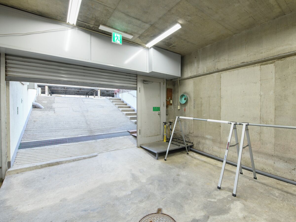 A concrete interior with a metal staircase leading to an upper level, a metal ladder, and a green exit sign.